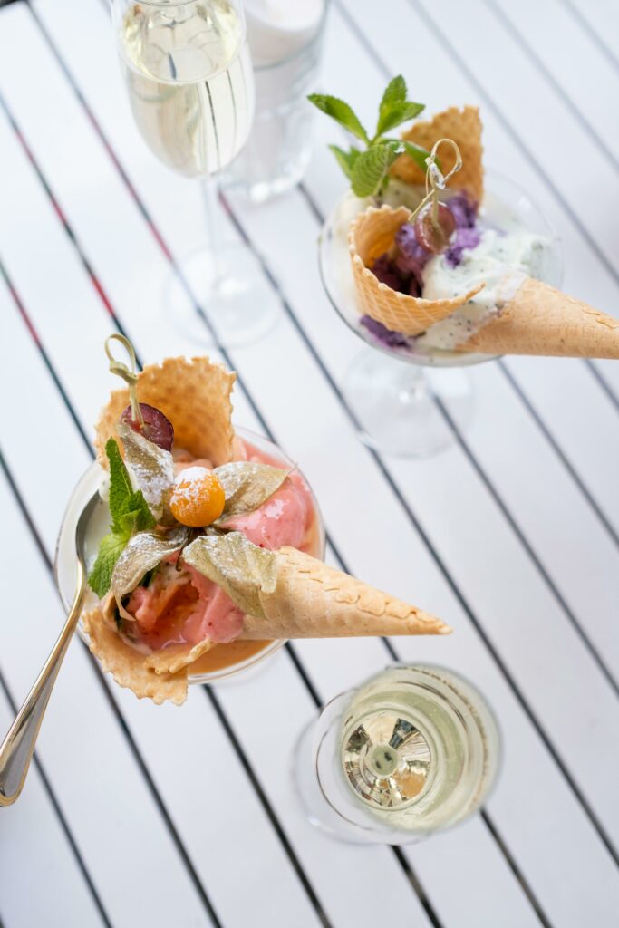 Ice cream cones with mint leaves and fruit on a striped table beside glasses of champagne.